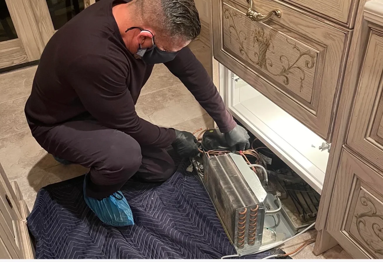 Technician repairing the compressor and coils of a refrigerator pulled out from the cabinetry